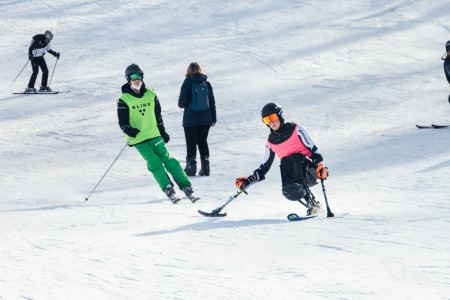 Many people are skiing down the hill on a ski slope. In the foreground is a person on a monoski.