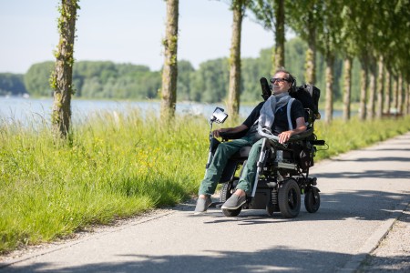 A man rides an electric wheelchair along a lake.