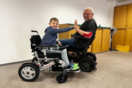Foto von zwei Personen, ein Kind und ein Erwachsener, sitzen im Rollstuhl FreedomChair A11 und klatschen sich ab.