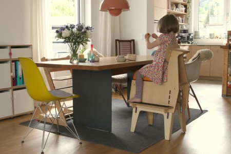 Foto des Sitzmöbel Rückwärtsreiter aus Holz, auf dem ein Kind am Esstisch sitzt.