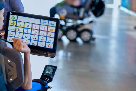 A wheelchair user operates a tablet with a voice assistance system.