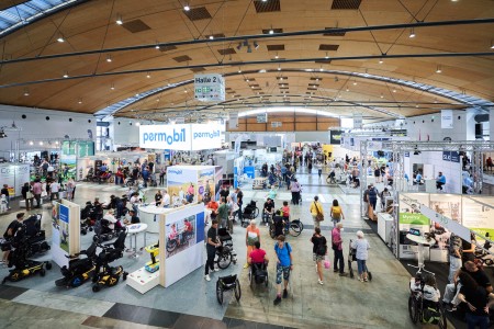 In an exhibition hall, many exhibitors present wheelchairs at exhibition stands. 